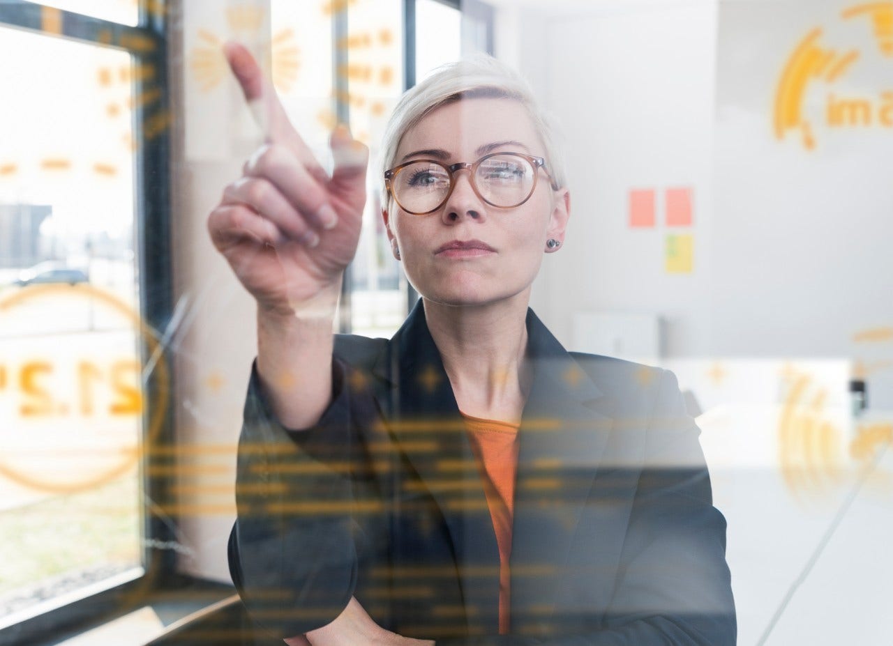 1166413488 Businesswoman touching glass wall with data in office
