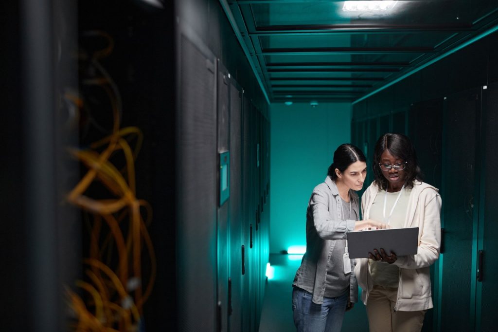 Wide angle portrait of two female IT engineers setting up server network while working in data center, copy space