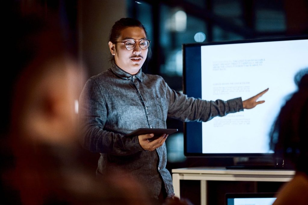 1153350345 Shot of a young businessman delivering a presentation during a late night meeting at work