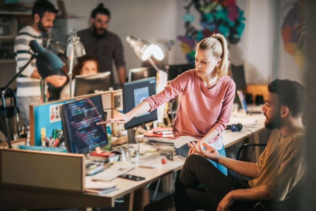 1157345255 Group of computer programmers working in the office. Focus is on blond woman showing something to her colleague on PC.