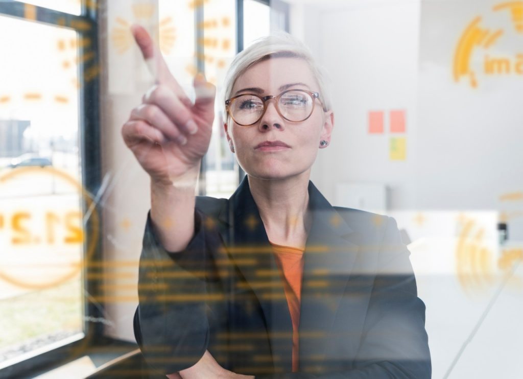 1166413488 Businesswoman touching glass wall with data in office