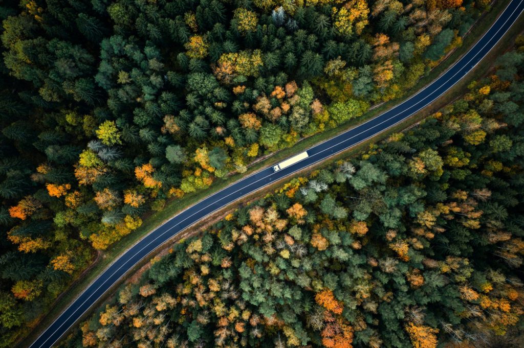 1281145596 Arial view of heavy truck on a narrow twisting road. Autumn colorful trees by the sides of the road.