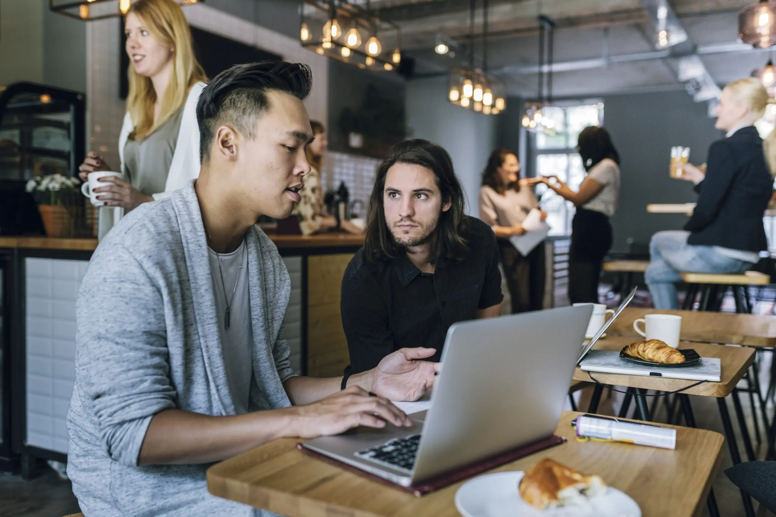 Two young entrepreneurs sitting in a busy business cafe, working and discussing projects and ideas.
